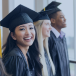 Group of smiling graduates in caps and gowns standing by a window.
