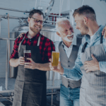 Three generations of family business owners smiling and holding beer in a brewery, symbolizing legacy, teamwork, and succession planning.