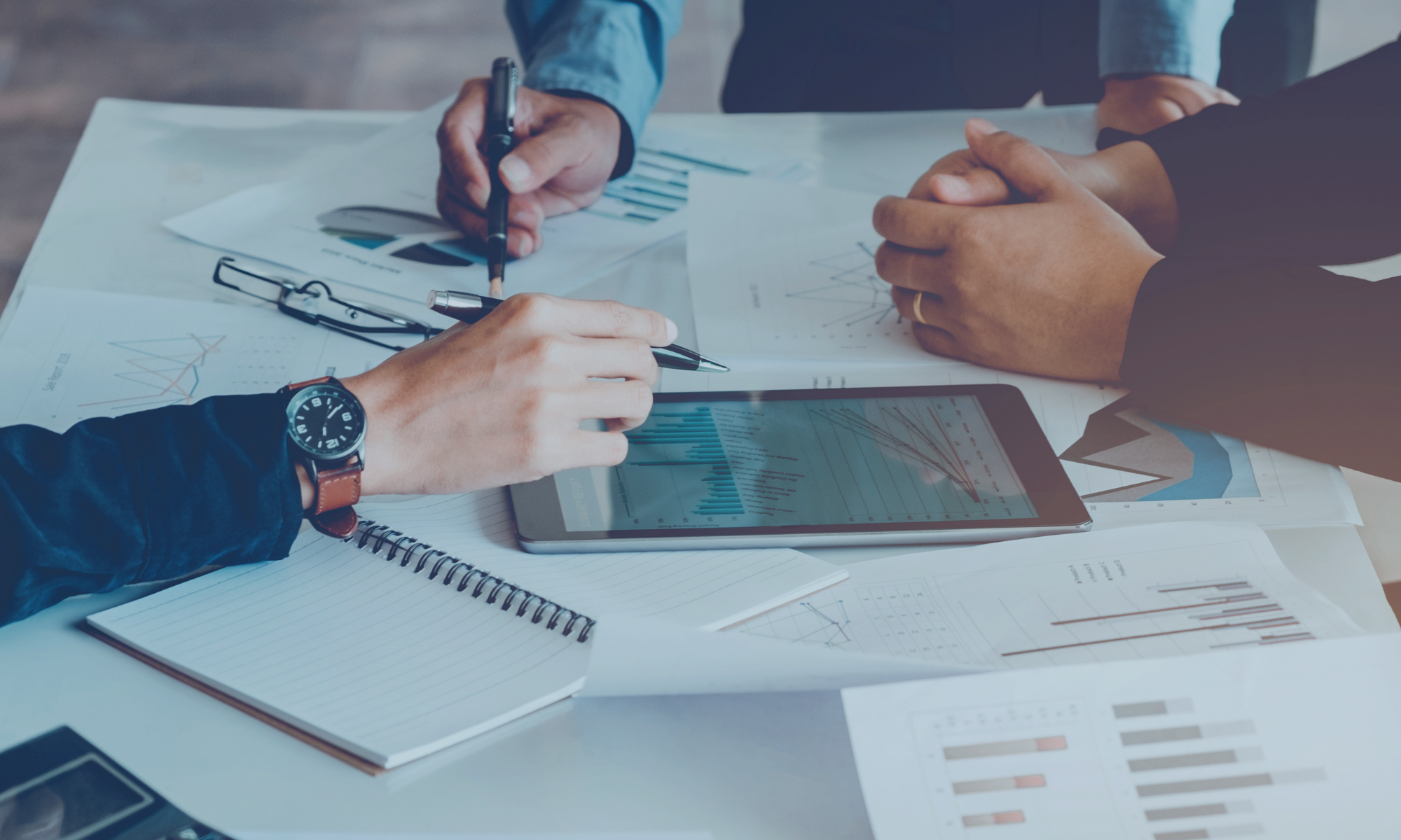 Business professionals analyzing financial data and performance metrics on tablet and printed charts during a strategy meeting.