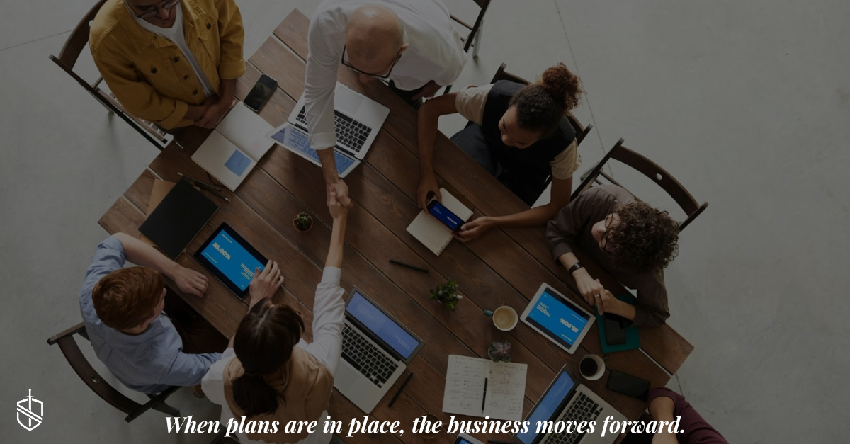 Overhead view of a diverse business team meeting around a table, collaborating on laptops and tablets, symbolizing succession planning, teamwork, and business continuity.