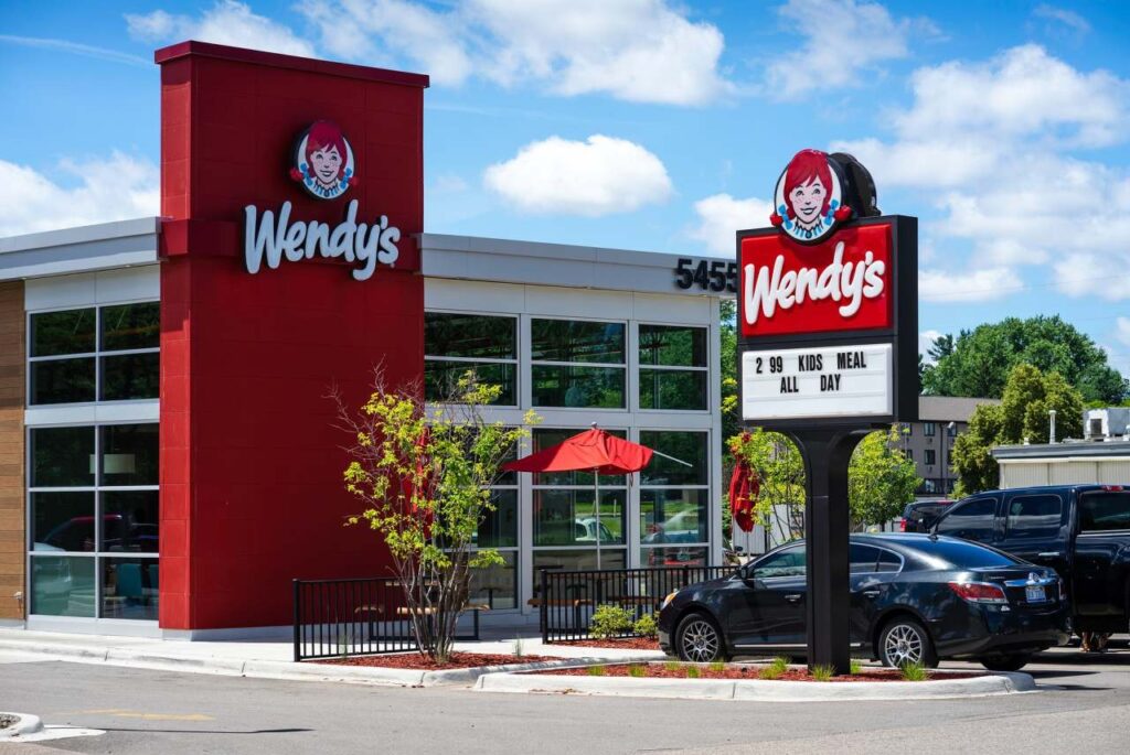 Exterior of a Wendy’s fast food restaurant with red signage, large windows, and a roadside sign advertising a kids meal.