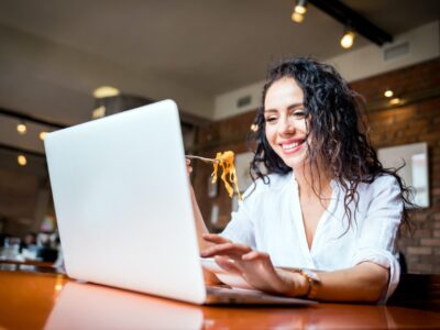 Latin young woman working on laptop computer at restaurant, eating break during work